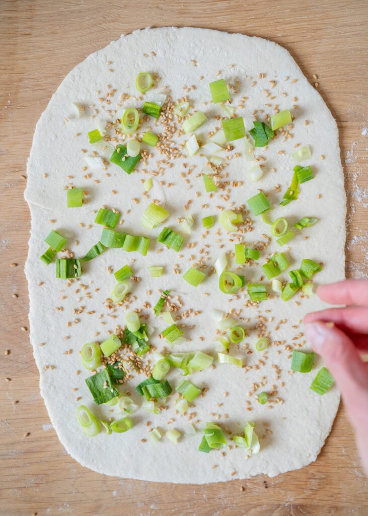 sprinkled scallions and toasted sesame seeds on rolled out dough rectangle