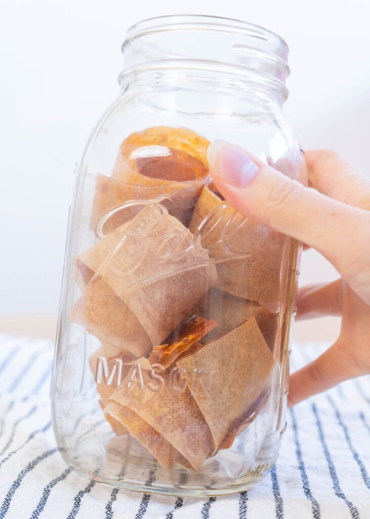 jar of homemade baked fruit leather cut into strips and rolled